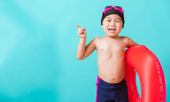 Summer vacation concept, Portrait Asian happy cute little child boy wear goggles and swimsuit hold watermelon inflatable ring, Kid having fun on summer vacation, studio shot isolated blue background