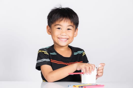 Little cute kid boy 5-6 years old smile using pencil sharpener while doing homework in studio shot isolated on white background, Asian children preschool sharpening color pencils, education concept