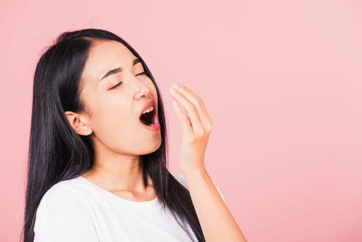 Portrait Asian beautiful young woman emotions tired and sleepy her yawning covering mouth open by hand, studio shot isolated on pink background, Thai female insomnia concept