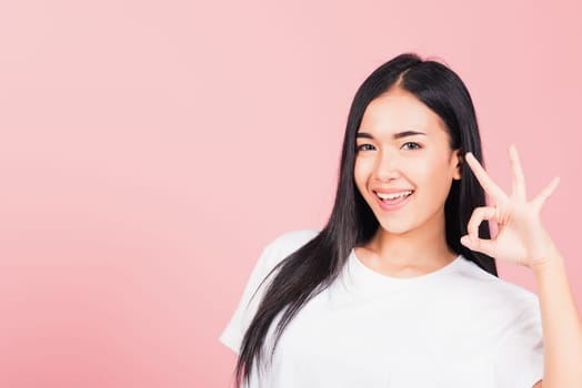 Portrait Asian beautiful young woman standing, She made finger OK symbol sign to agree side away looking at camera, studio shot isolated on pink background, Thai female agree hand sign copy space