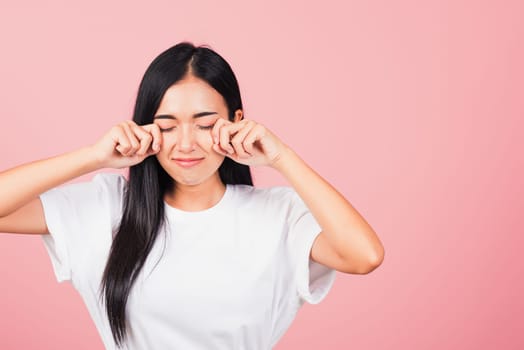 Asian portrait beautiful cute young woman bad mood her cry wipe tears with fingers, studio shot isolated on pink background, Thai female feeling sad unhappy crying with copy space