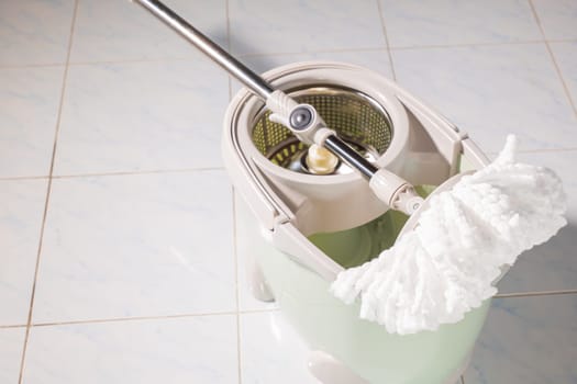 Mop with microfiber head spinning on the bucket next to floor cleaning liquid and mopping the floor house in the living room