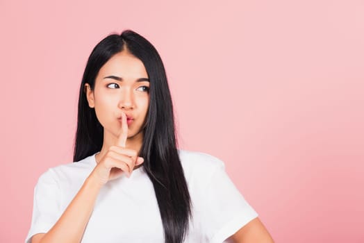 Asian happy portrait beautiful cute young woman smile stand making finger on lips mouth silent quiet gesture studio shot isolated on pink background, Thai female looking to side away with copy space