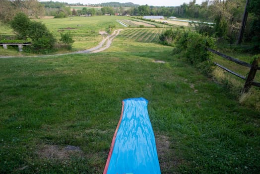 greenhouses and dirt roads in the agricultural background. View from the top of a child's slipping sliding toy on a grassy hillside. Idyllic scene with rolling hils and nature background shot in natural light with no people and copy space.