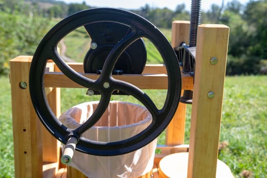 Family farm wooden apple cider press on a grassy hill with a closeup of the flywheel. No people.
