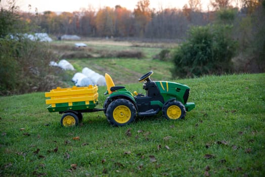 nostalgic family image of childs riding toy tractor in an idyllic nature background scene with green grass and agricultural fields.