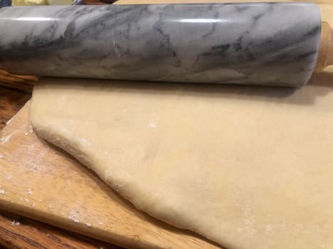 Closeup of traditional rustic kitchen bakery wooden countertop, and cutting board with tender dough rolled out and swirled granite rolling pin. Warm cozy lighting for artesanal feel, no people, with copy space
