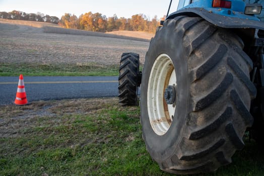 Off center large tractor tire with tread in foreground and golden hour autumn farm field nature background. Field is freshly harvested and trees with autumn foliage against horizon.