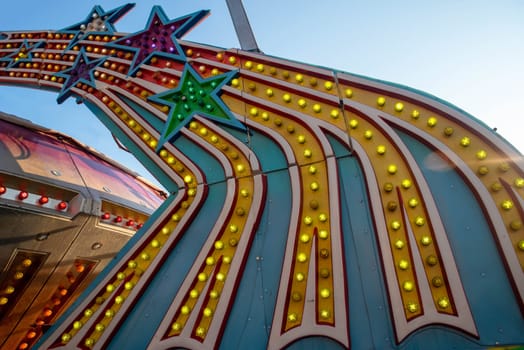 bold bright colorful light bulbs on amusement park ride shaped like shooting stars shot outdoors in natural light blue sky background with copy space