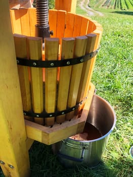 Idyllic green farm nature background with old fashioned cider press foreground. Cider pours from the press into a metal cooking pot sitting on a grassy hillside in natural light with no people.