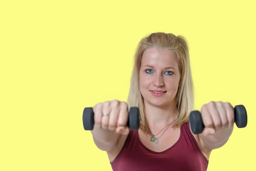 Studio shot of attractive young woman posing  with a dumbbells on yellow background.