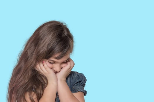 Ashamed tanned long haired little girl wears  denim costume is posing on cyan background.