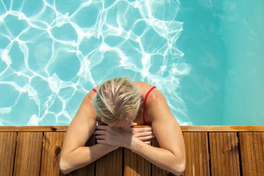 Top view of woman standing in swimming pool and leaning on wooden edge.