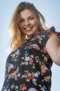 Bottom view of attractive beautiful young woman standing outdoors against blue sky and smiling at the camera.