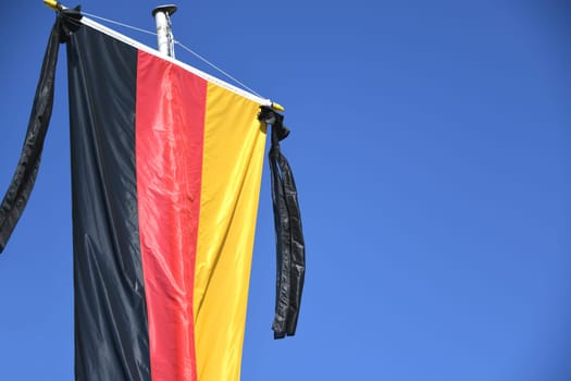 The national flag of the Federal Republic of Germany,black,red and gold,hangs on the flagpole. As a symbol of national mourning,the mourning ribbon is attached to the flag with two black ribbons.