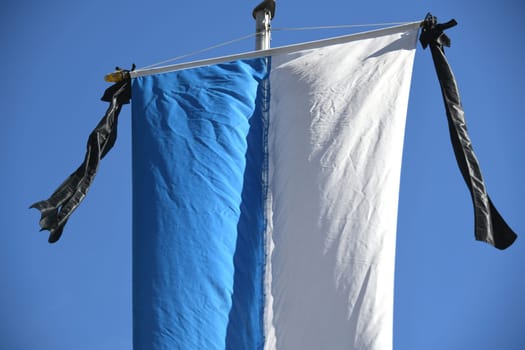 The white,blue flag of the state of the Federal Republic of Germany,Bavaria,hangs on the flagpole. As a symbol of mourning,the black ribbon is attached to the flag with two black ribbons.