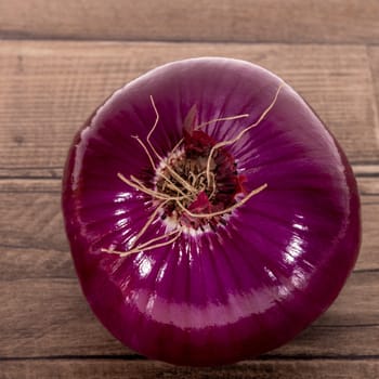 Single whole vegetable of red onion on a wooden kitchen board, close up