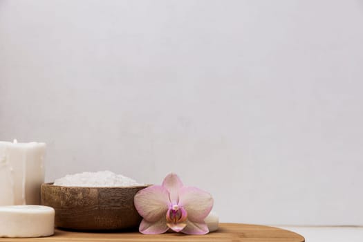 Preparation for hotel spa treatment, home bath procedure. Gray washbasin in bathroom, accessories on wooden tray. Burning candle, sea salt in bamboo bowl, orchid flower, homemade eco soap