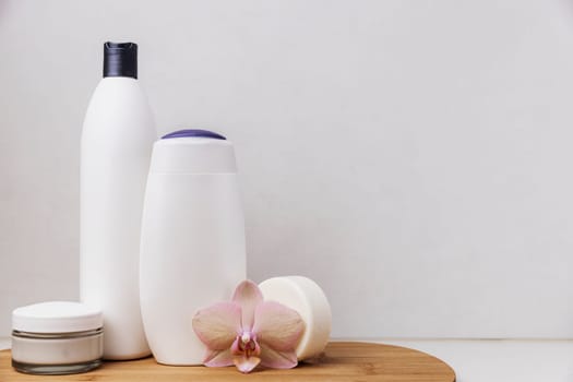 Preparation for hotel spa treatment or home bath procedure. Bathroom accessories and cosmetics on wooden tray. Shampoo and conditioner, shower gel, soap, cream glass bottle, white soap, orchid flower