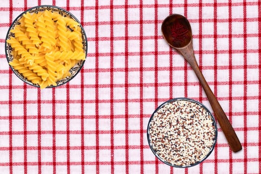 Vegetable food. Closeup of two bowls with noodles and quinoa and a spoon with safran spice threads on a tablecloth. Healthy eating and nutrition. Top view with space.