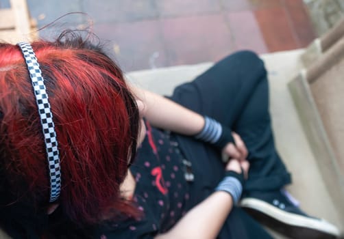 Punk emo girl, young adult with black red hair, sitting at a window frame, looking down, high angle view, horizontal