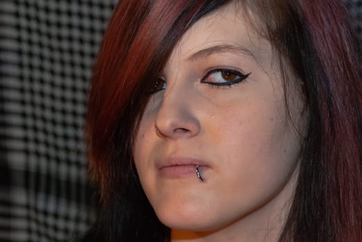 Young punk emo Girl with piercing, with red and black hair, looking at camera with serious facial expression, close-up