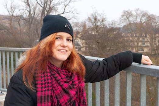 Young alternative punk emo girl smiling, looking at camera while standing on a observation point with bad kreuznach, germany in the background, horizontal