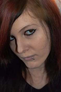 Young punk emo Girl with piercing, with red and black hair, looking at camera with serious facial expression, close-up