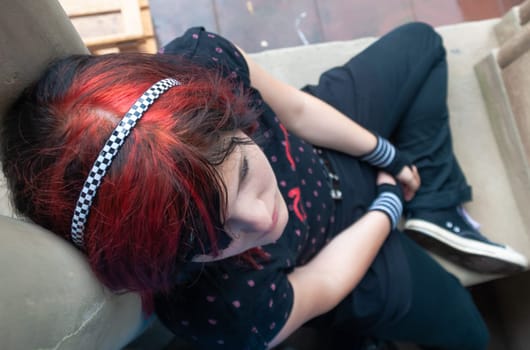Punk emo girl, young adult with black red hair, sitting at a window frame, looking up, high angle view, horizontal