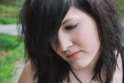 Gothic emo girl looking down with thoughtful facial expression, black hair, close-up