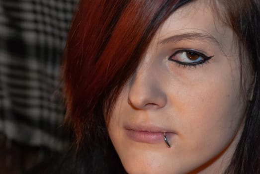 Young punk emo Girl with piercing, with red and black hair, looking at camera with serious facial expression, close-up