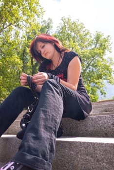 Punk emo girl, young adult with black red hair, sitting on a staircase outdoors, looking down, low angle view, vertical