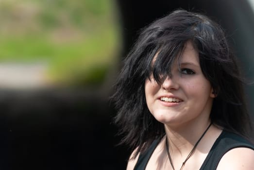 Punk emo girl, young adult with black hair and eyeliner, smiling, looking at camera, outdoors, horizontal, close-up