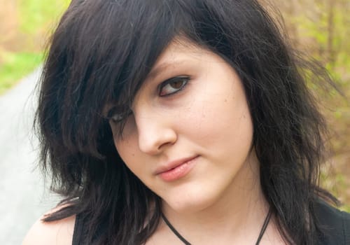 Punk emo girl, young adult with black hair and eyeliner, looking at camera, outdoors, close-up, horizontal