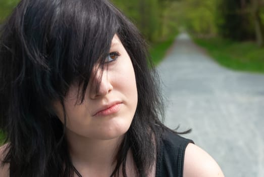 Punk emo girl, young adult with black hair and eyeliner, looking away, outdoors, close-up, horizontal