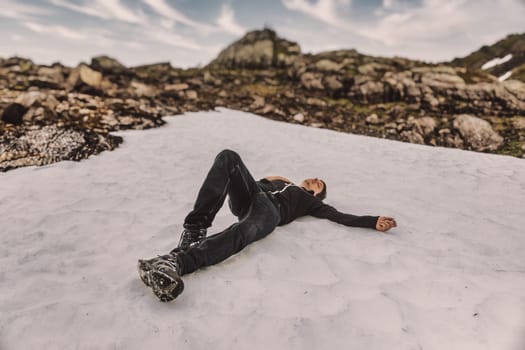Young adult man is exhausted and relaxes after hiking to the top of a mountain in norway, lying down in the snow putting his hand on his breast