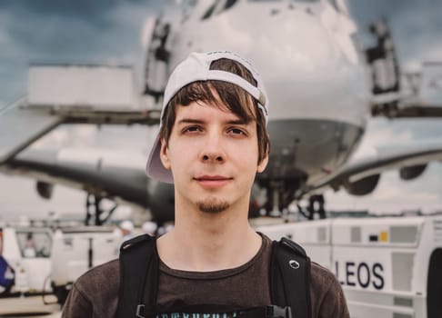 Young adult man passenger looking at camera while standing in front of a big airplane at the airport