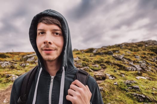 Young adult man with brown hair and beard hiking on top of a mountain, wearing a backpack, looking at camera, autumn, volda, norway