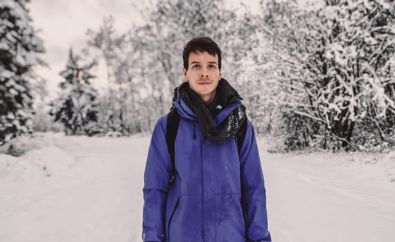Young adult man with brown short hair standing at beautiful snow landscape during winter in norway, wearing a blue rain jacket, looking at camera, norway