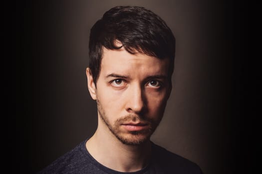 Young adult man with brown hair and beard with sceptic anger facial expression looking at camera