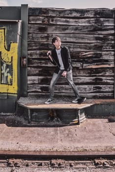 Young adult singer, with brown long hair and beard performing, rock musician with microphone outdoors in front of a wooden wall, standing, looking away, wearing jeans and t-shirt
