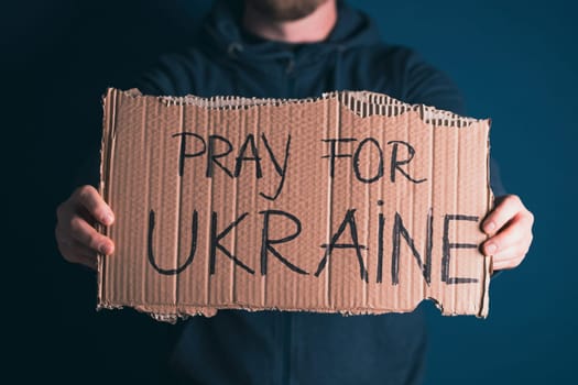 Man holding Pray for Ukraine banner. Concept symbol of help support and no war in the country of Ukraine.