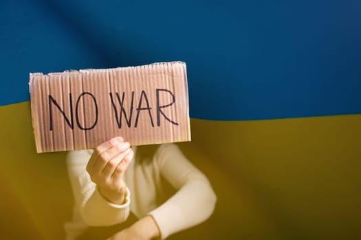 Sad woman calls to Stop war in Ukraine, raises banner with inscription No war over ukrainian flag