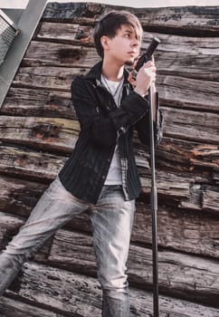 Young adult singer, with brown long hair and beard performing, rock musician with microphone outdoors in front of a wooden wall, standing, looking away, wearing jeans and t-shirt