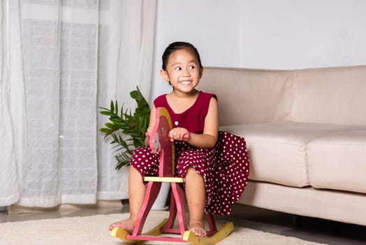 Asian cute little girl swinging riding toy horse, Smiling kid playing horse rocking chair at home in living room, Happy time to play during self kindergarten preschool