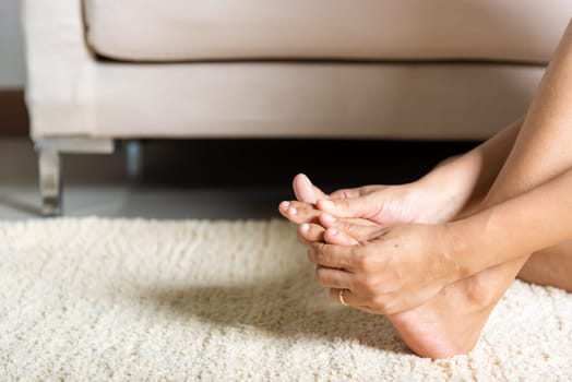 Foot pain, Asian woman holds her toe injury feeling pain her foot at home, female suffering from feet ache use hand massage relax muscle from toe in house interior, Healthcare problems medical concept