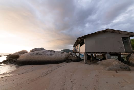 Old wooden house near the beach and rock in dramatic sunset
