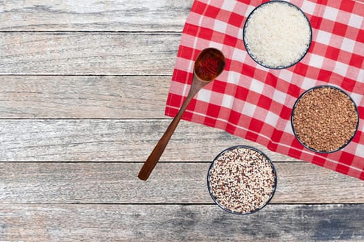 Vegetable food. Closeup of three bowls with rice, buckwheat and quinoa and a spoon with safran spice threads on abstract blurred table. Healthy eating.Top view with space.