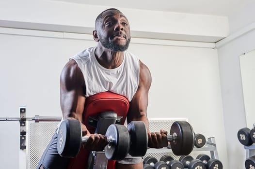 An African-American man shakes his biceps on an inclined bench in the gym. High quality photo