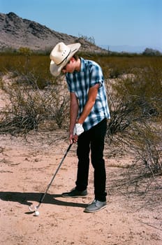 Young boy in natural terrain desert golfing